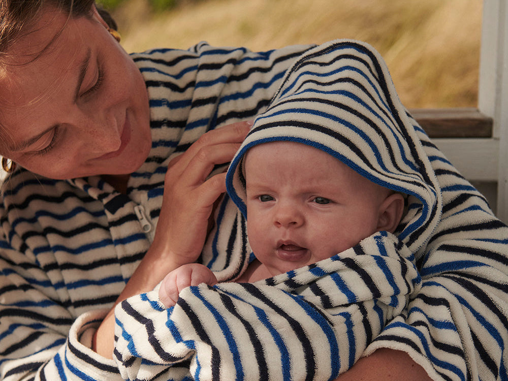 Nyfödd baby insvept i randig handduk med huva i en förälders famn