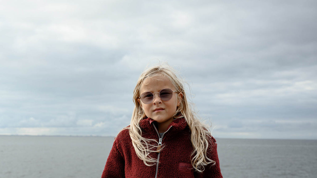 Barn i vinröd teddyfleecejacka vid havet en grå septemberdag