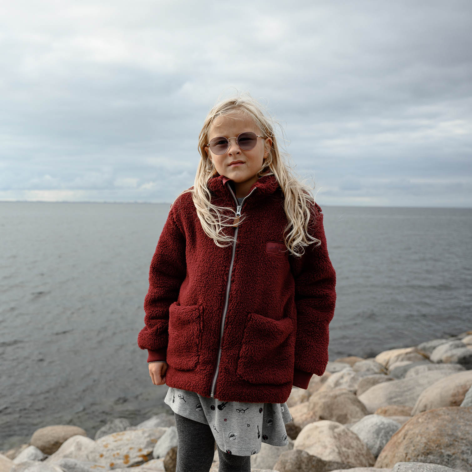 Barn i vinröd teddyfleecejacka vid havet en grå septemberdag